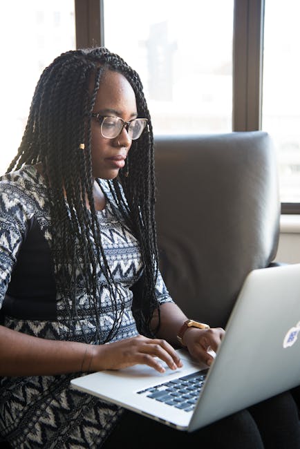 Focused young woman typing on laptop in a contemporary workspace.